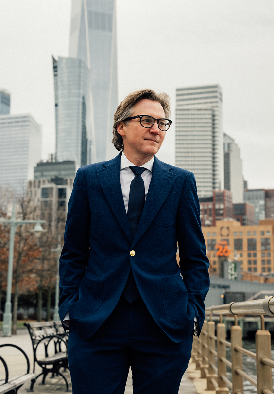 Doctor Craig Baldenhofer MD in navy suit and glasses standing confidently with city skyline background - Doctor in New York, NY