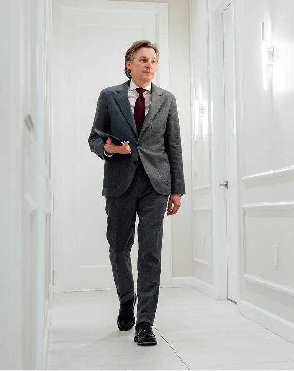 Doctor Craig Baldenhofer MD in gray suit walking through modern white hallway holding mobile phone - in New York, NY