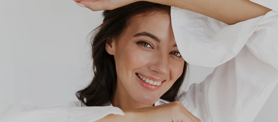 Woman with glowing skin smiling while touching her face, demonstrating healthy skincare routine and natural beauty - Energy in New York, NY