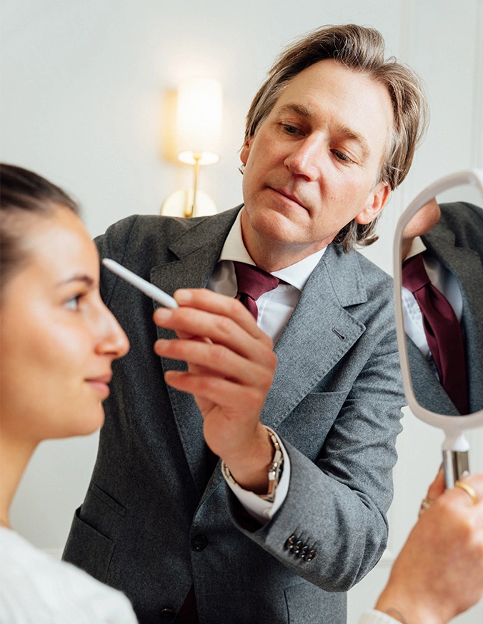 Doctor Craig Baldenhofer MD marking a patients forehead while she holds a mirror in front of her face. - Brow lift in New York, NY