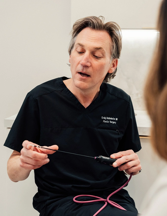 Doctor Craig Baldenhofer MD holding medical tool and his hand and explaining to the patients. - Liposuction in New York, NY