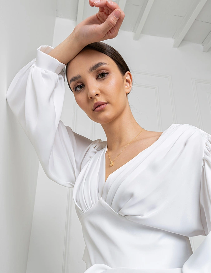 Woman in elegant white puff sleeve blouse posing with hand raised against modern architectural background - Lower eyelid in New York, NY