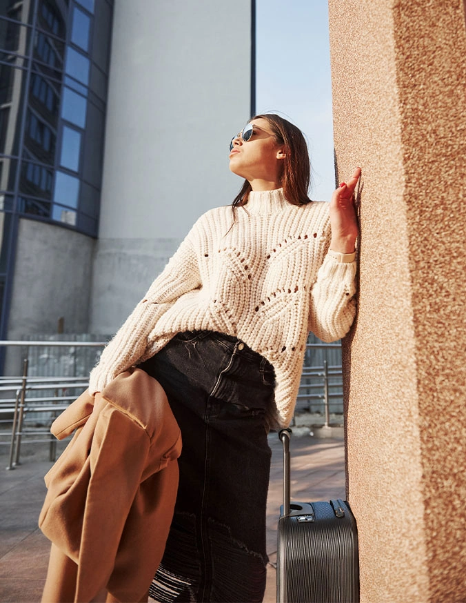 Woman in cream knit sweater and black pants leaning against pillar outdoors in urban setting - Out of town in New York, NY